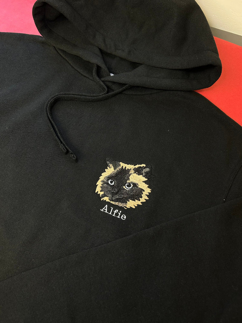 Black hoodie with embroidered cat design and 'Alfie' text on a red surface