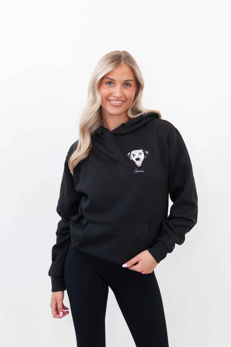 A woman wearing a black hoodie with a custom embroidered pet portrait on the front.